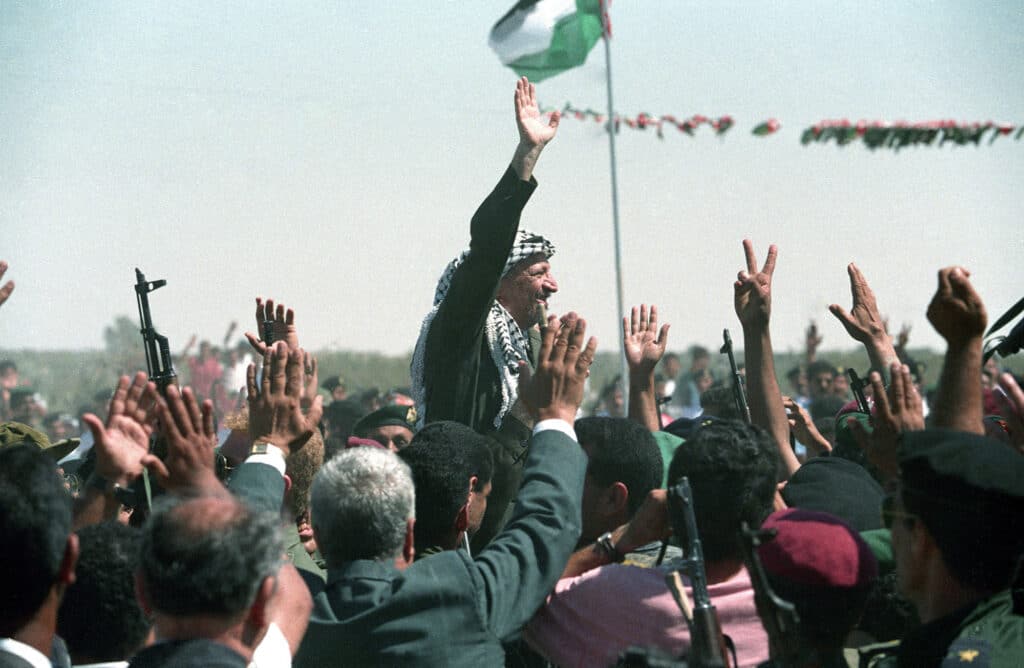 PLO chairman Yassir Arafat waves to a crowd of cheering Palestinians as he is carried on shoulders after he crossed the Rafah border point, entering tye newly self-ruled Gaza strip for the first time in 27 years on July 1, 1994 © Manoocher Deghati