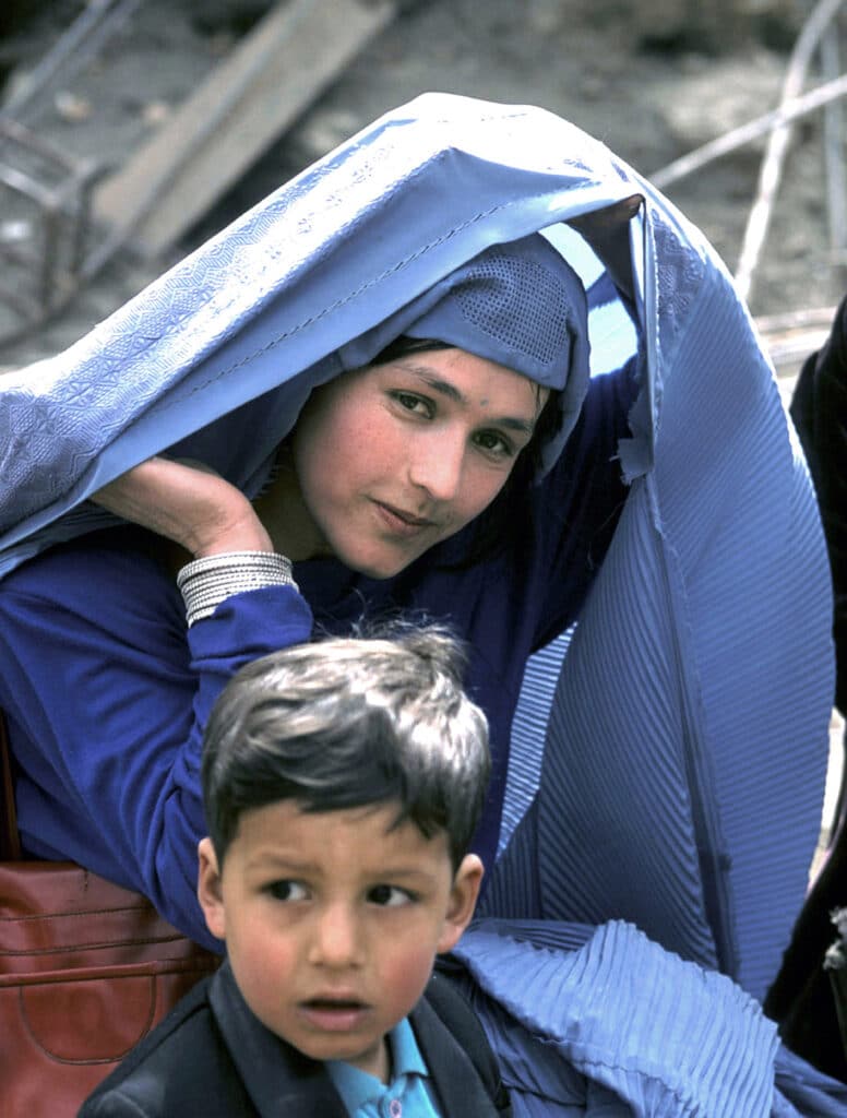 Kabul, Afghanistan, 2002: An Afghan woman lifts her veil while bringing her son to school in Kabul for the first time after the fall of Taliban in 2002. Even before the Taliban made the burqa obligatory, the all-enveloping garment was very widespread in this highly conservative Central Asian country © Manoocher Deghati