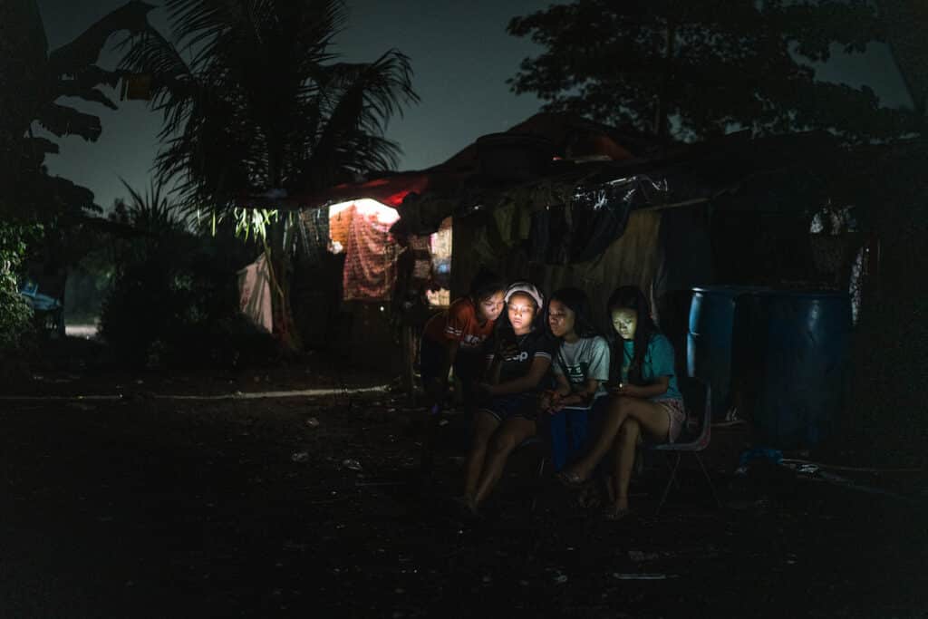 Young girls in Manila are seen with their mobile phones during a community blackout. © Hannah Reyes Morales