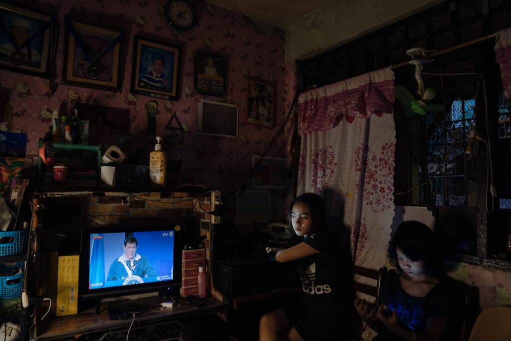 Students review their online school work at home, as Duterte makes a speech on television. © Hannah Reyes Morales