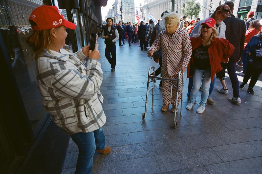 Trump Supporter Taking a photo of a friend posing with a Trump opponent at the Donald Trump Rally at Madison Square Garden. New York City. October 27, 2024 © Robert E. Gerhardt