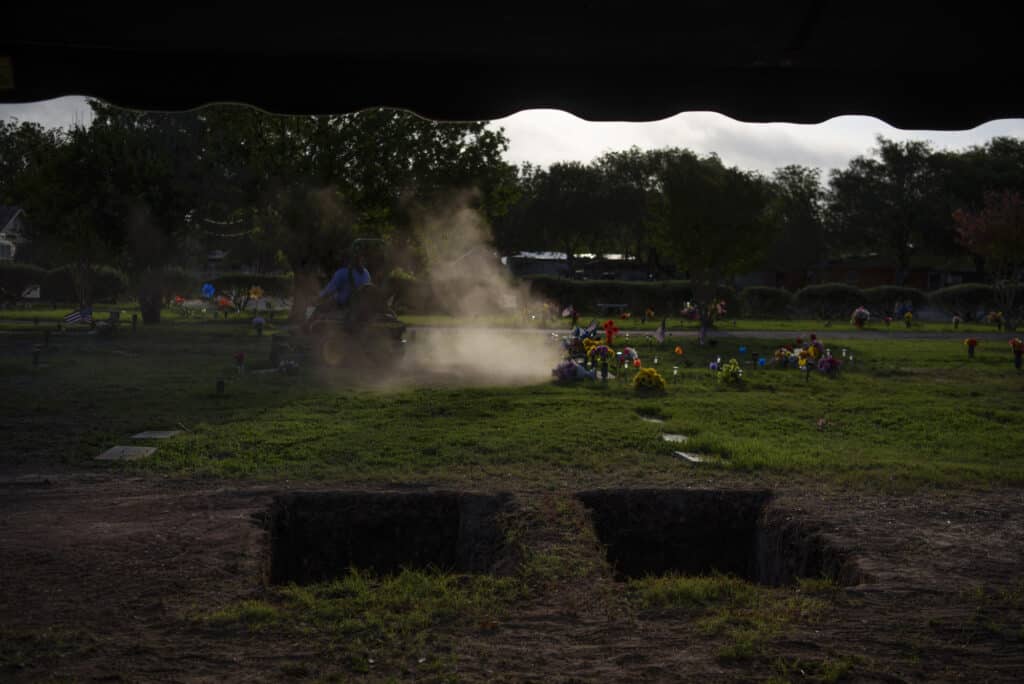 June 1st, 2022. Uvalde, Texas. A man mows the grass around two graves, which will hold the remains of Irma Garcia, who was killed during a mass shooting at Robb Elementary School, and her husband, Joe Garcia, who died of a heart attack two days later, at Hillcrest Memorial Cemetery. © Callaghan O’Hare for The New York Times