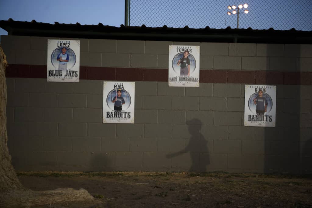 June 16th, 2022. Uvalde, Texas. A child’s shadow is cast among posters honoring the members of Little League who died in a mass shooting at Robb Elementary School, which left 19 children and two adults dead, as the town of Uvalde hosts the Texas Little League District 21 All-Star tournament. © Callaghan O’Hare for The New York Times