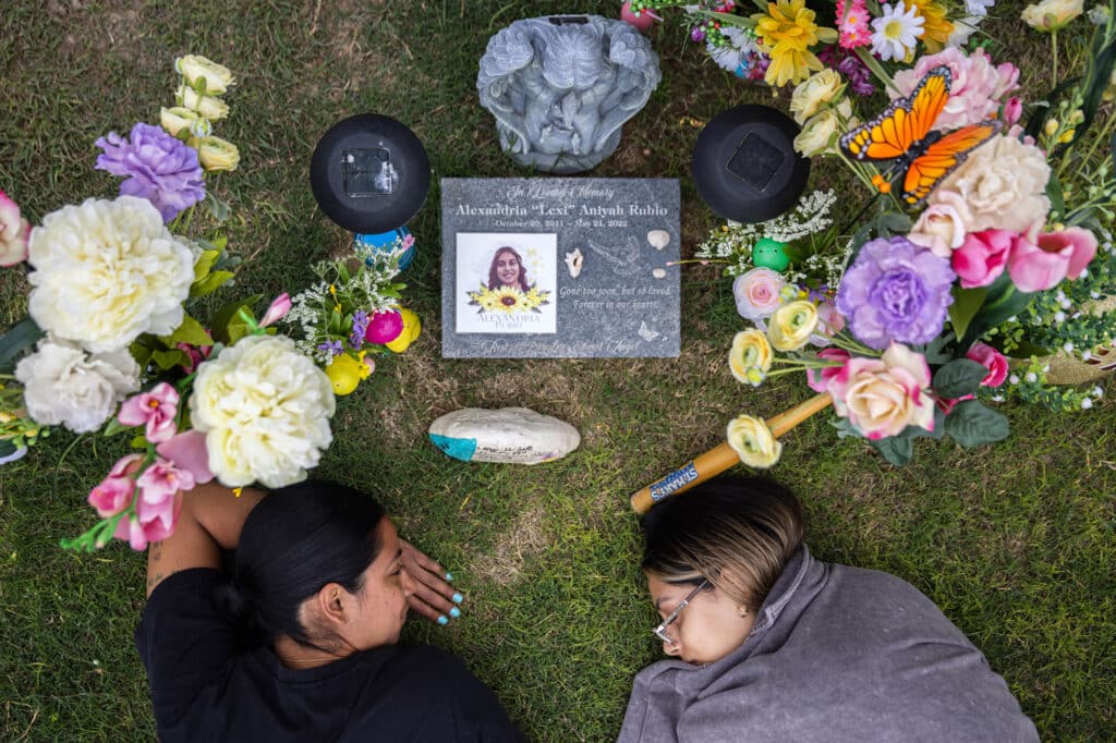 Kimberly Rubio and her oldest daughter, Kalisa Barboza, lay in the grass at Lexi’s grave after getting tattoos in her honor in Uvalde, Tex., on April 6, 2023. (Tamir Kalifa)